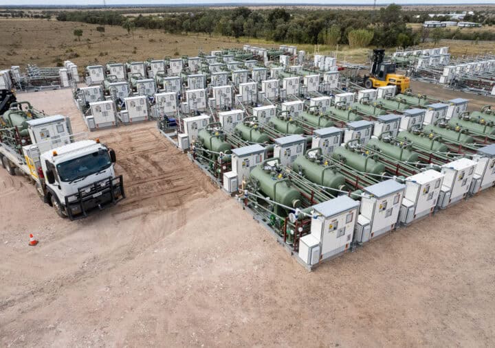 A large truck parked beside a large storage tank in an industrial setting.