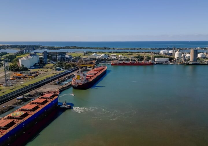 Aerial view of a busy port featuring several ships and a large building along the waterfront.