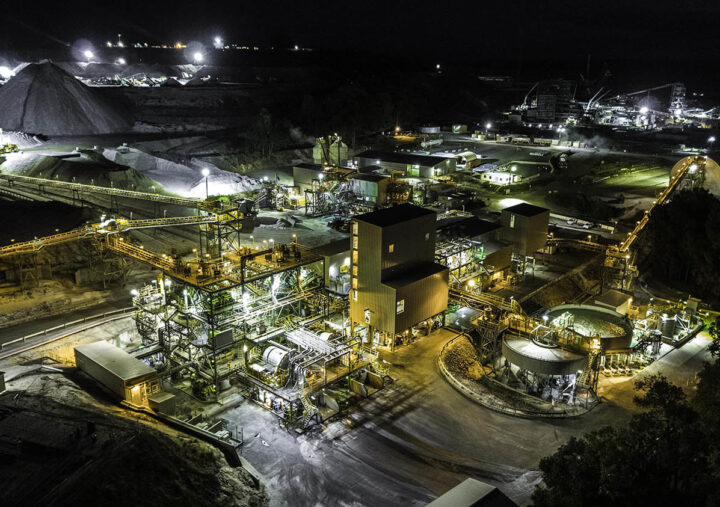 Aerial view of a coal mine illuminated at night, showcasing machinery and mining structures against a dark landscape.