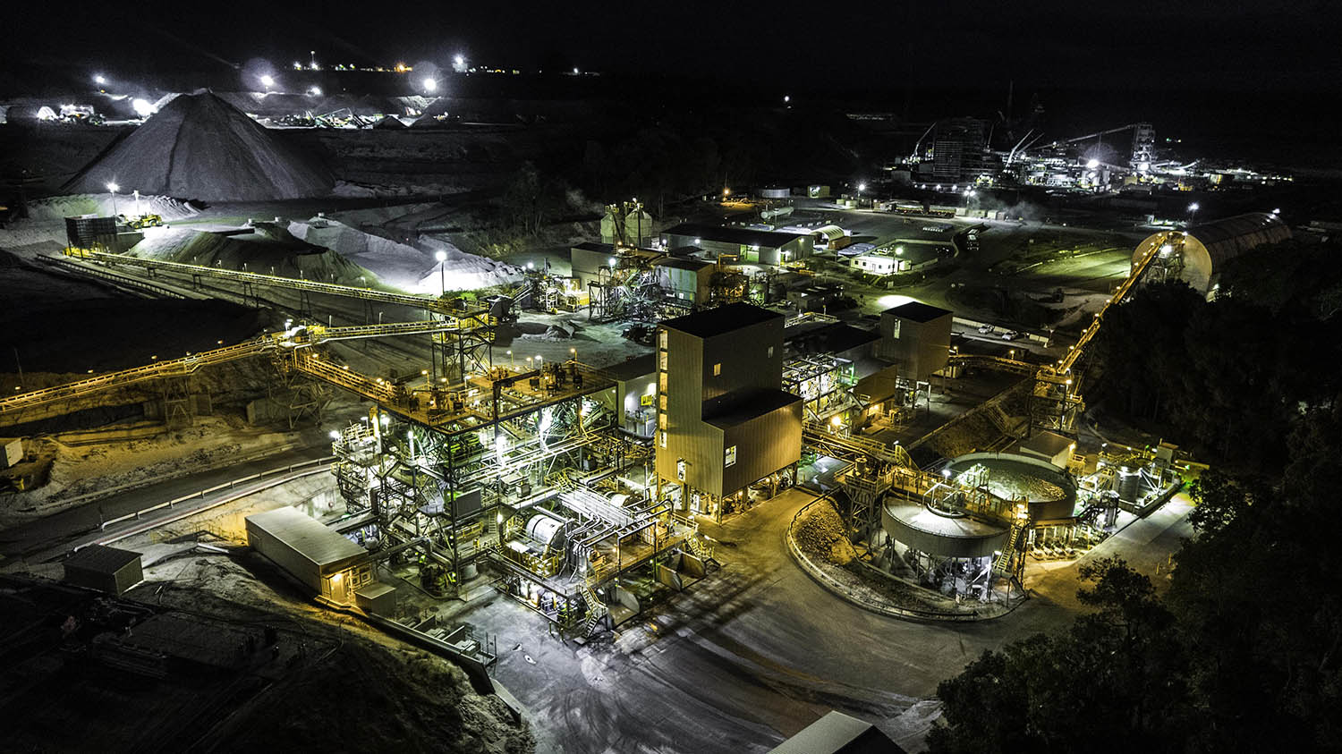 Aerial view of a coal mine illuminated at night, showcasing machinery and mining structures against a dark landscape.